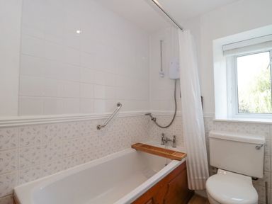 A bathroom with a bathtub a shower curtain a window and a toilet at Abbey Cottage Montacute