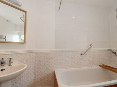 A bathroom with a bathtub with a wooden tray a handrail a sink a mirror and tiled walls at Abbey Cottage Montacute