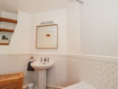 A bathroom with a pedestal sink mirror above and tiled walls at Abbey Cottage Montacute