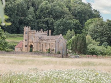 A stone castle surrounded by trees and fields with wildflowers at Abbey Cottage Montacute in Montacute