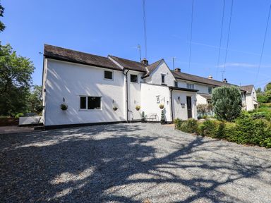A white exterior house with a gravel driveway and plants at Ellerbeck Bridge in Underbarrow near Kendal