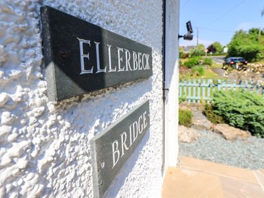 A close up of house name plaques on a wall with a garden and road in the background at Ellerbeck Bridge in Underbarrow near Kendal