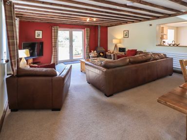 A living room with brown leather sofas a wood burning stove and a television at Ellerbeck Bridge in Underbarrow near Kendal