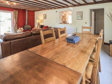 A dining area with wooden chairs and table facing a living room with a leather sofa and wood stove at Ellerbeck Bridge in Underbarrow near Kendal