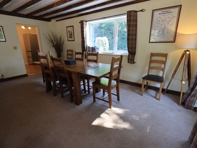 A dining room with a wooden table and chairs near a window and a lamp at Ellerbeck Bridge in Underbarrow near Kendal