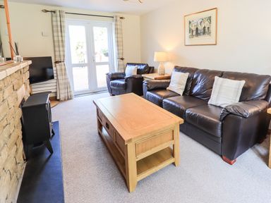 A living room with leather sofa and armchair wooden coffee table and stone fireplace at Ellerbeck Bridge in Underbarrow near Kendal