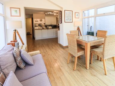 A dining area with wicker chairs and glass table next to a sofa and a kitchen in the background at Ellerbeck Bridge in Underbarrow near Kendal