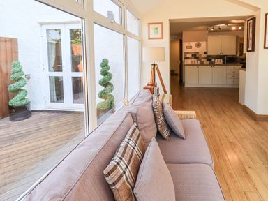 A living area with a sofa and cushions next to large windows showing an outdoor deck and topiary at Ellerbeck Bridge Underbarrow near Kendal