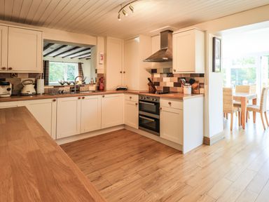 A kitchen with white cabinets wooden countertops and a dining area with wicker chairs at Ellerbeck Bridge in Underbarrow near Kendal
