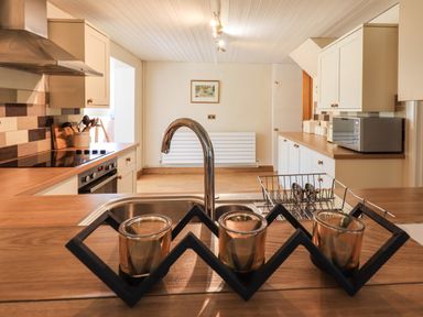 A kitchen with a sink faucet countertop cabinets stove and microwave at Ellerbeck Bridge in Underbarrow near Kendal
