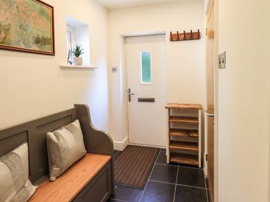 An entrance hall with a bench and cushions a door with a mail slot a small wooden shelf and hooks at Ellerbeck Bridge in Underbarrow near Kendal