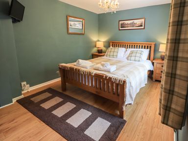 A bedroom with a wooden bed with pillows and towels bedside tables with lamps and a television on the wall at Ellerbeck Bridge Underbarrow near Kendal