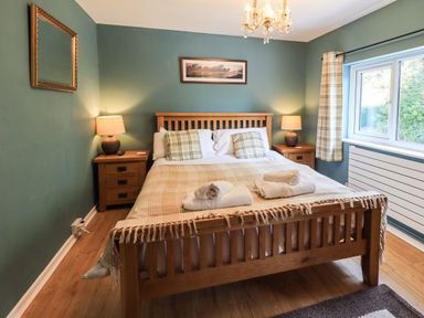 A bedroom with a wooden bed a blanket pillows bedside tables lamps a window and a mirror at Ellerbeck Bridge in Underbarrow near Kendal