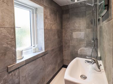 A bathroom with a white sink and chrome faucet a walk-in shower with a rain showerhead and a window with toiletries on the sill at Ellerbeck Bridge in Underbarrow near Kendal