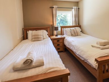 A bedroom with two single beds separated by a wooden nightstand with a lamp at Ellerbeck Bridge in Underbarrow near Kendal
