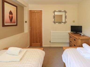 A bedroom with two single beds with white linens a wooden door a wooden dresser with a television and a mirror on the wall at Ellerbeck Bridge in Underbarrow near Kendal
