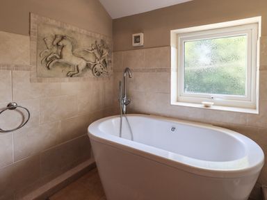 A bathroom with a bathtub under a window and a horse and chariot mural on the wall at Ellerbeck Bridge in Underbarrow near Kendal