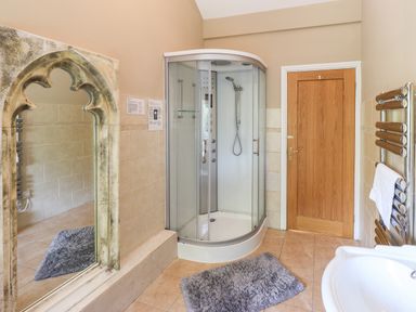 A bathroom with a corner shower cabin a large arched mirror a wooden door a towel radiator and a sink at Ellerbeck Bridge in Underbarrow near Kendal