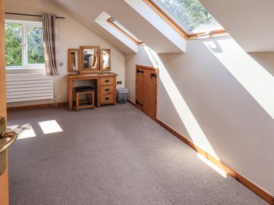A room with a wooden dressing table and stool next to windows with sunlight coming in at Ellerbeck Bridge in Underbarrow near Kendal