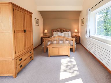 A bedroom with a wooden bed frame two bedside tables with lamps a wooden chest and a wooden wardrobe at Ellerbeck Bridge in Underbarrow near Kendal