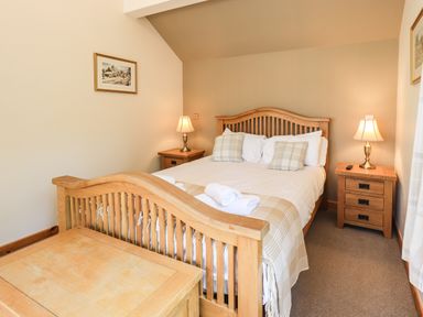 A bedroom with a wooden bed and bedside tables with lamps at Ellerbeck Bridge in Underbarrow near Kendal