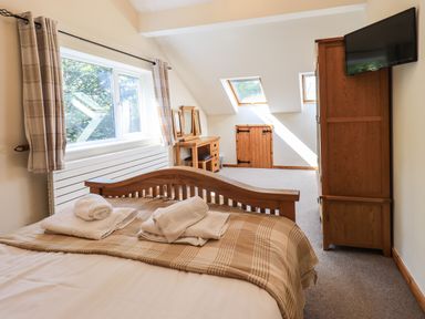 A bedroom with a wooden bed a dresser a wooden wardrobe and windows at Ellerbeck Bridge in Underbarrow near Kendal