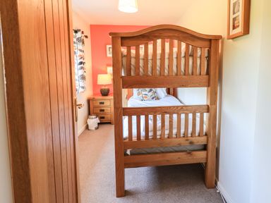 A bedroom with a wooden bunk bed a bedside table with a lamp and a window with patterned curtains at Ellerbeck Bridge Underbarrow near Kendal