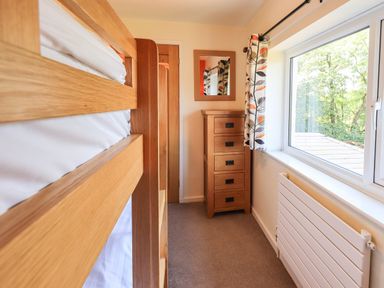 A bedroom with a wooden bunk bed a wooden chest of drawers with a mirror and a window with patterned curtains at Ellerbeck Bridge Underbarrow near Kendal
