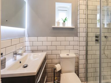 A bathroom with a sink, toilet, shower enclosure, and small window with plant at Ellerbeck Bridge in Underbarrow near Kendal
