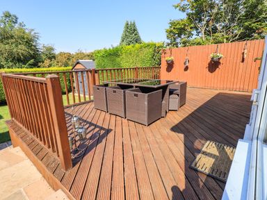 An outdoor wooden deck with brown wicker furniture and a railing at Ellerbeck Bridge in Underbarrow near Kendal
