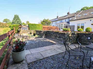 A backyard with stone walls patio furniture potted plants a wooden fence and a small garden shed at Ellerbeck Bridge in Underbarrow near Kendal