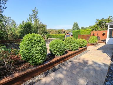 A garden with trimmed bushes paved pathway and wooden deck at Ellerbeck Bridge in Underbarrow near Kendal