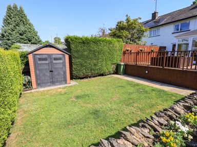 A backyard with a shed a patio a green lawn flower bed and a house at Ellerbeck Bridge in Underbarrow near Kendal
