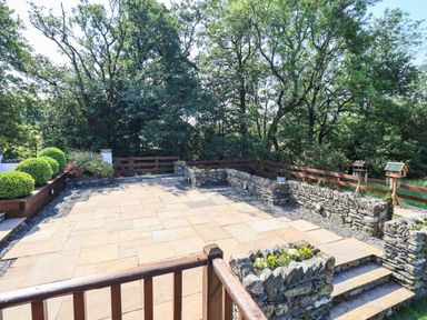 A stone paved patio with stone walls and greenery surrounded by trees at Ellerbeck Bridge in Underbarrow near Kendal