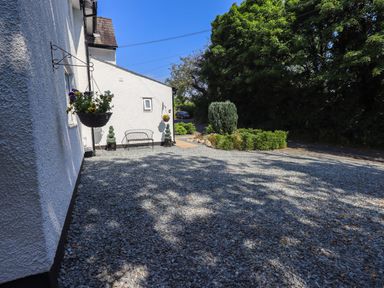 A gravel courtyard with a bench and hanging flower baskets at Ellerbeck Bridge in Underbarrow near Kendal