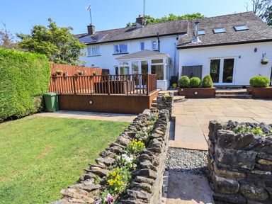 A backyard with a lawn stone path wooden deck and white house at Ellerbeck Bridge in Underbarrow near Kendal
