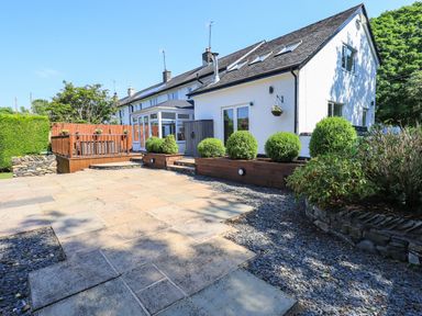 An outdoor patio area with stone tiles wooden deck and green bushes at Ellerbeck Bridge in Underbarrow near Kendal