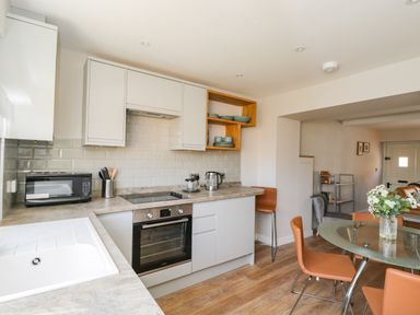 A kitchen with white cabinets a glass dining table with orange chairs and kitchen appliances at Troopers Cottage in Frome