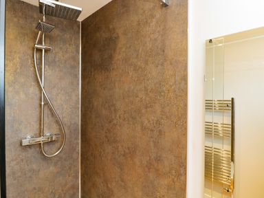 A shower area with a rain showerhead and a handheld showerhead next to a wall-mounted heated towel rail at Troopers Cottage in Frome