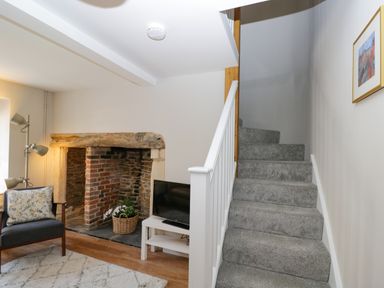 A living area with carpeted stairs a wooden chair a brick fireplace and a television at Troopers Cottage in Frome