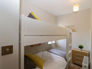 A small bedroom with white bunk beds yellow and gray pillows a wooden drawer with a plant and a radiator at Troopers Cottage in Frome