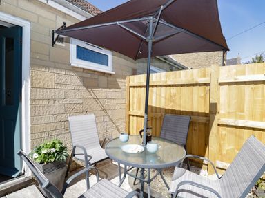 An outdoor patio with a round glass table four chairs a brown umbrella a flower pot and a wooden fence at Troopers Cottage in Frome