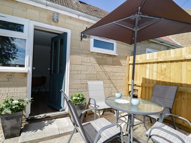 An outdoor patio with a glass table and four chairs under an umbrella at Troopers Cottage in Frome
