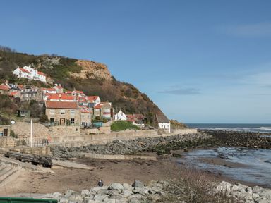 A coastal village with houses on a hillside beside a rocky shore and beach at Sea-u-Soon in Runswick Bay