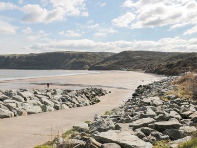 A coastal beach with a concrete path and rocks on both sides and hills in the background at Sea-u-Soon in Runswick Bay