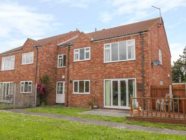 A brick two-story house with white framed windows a wooden fence and a small deck area at Sea-u-Soon in Runswick Bay