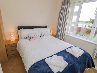 A bedroom with a bed two bedside tables with lamps and a window with curtains at Sea-u-Soon in Runswick Bay