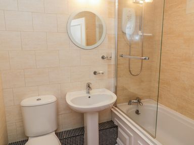 A bathroom with a toilet sink round mirror and bathtub with shower at Sea-u-Soon in Runswick Bay