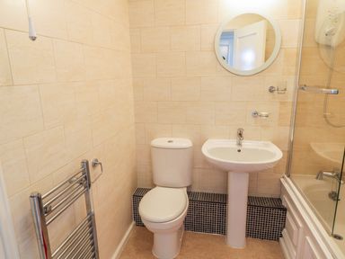 A bathroom with a toilet sink round mirror towel rail and a shower in Sea-u-Soon Runswick Bay