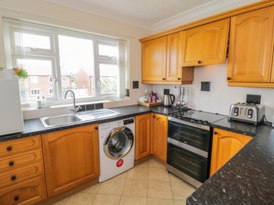 A kitchen with wooden cabinets a washing machine a stove a toaster and a sink under a window at Sea-u-Soon in Runswick Bay
